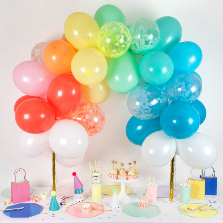 Arco di palloncini arcobaleno allestito su tavola di festa multicolor